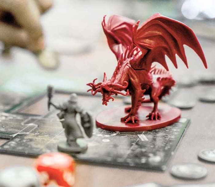 A cleric figurine stating in front of a red dragon on a gameboard of a tabletop fantasy roleplaying game
